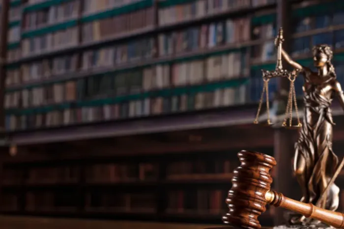 A dark, lawyerly image featuring a bronze statue of Lady Justice, holding scales and a sword, next to a wooden gavel.
