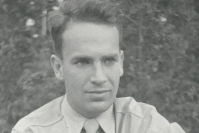 black and white outdoor portrait of a young man with neatly combed, short dark hair.