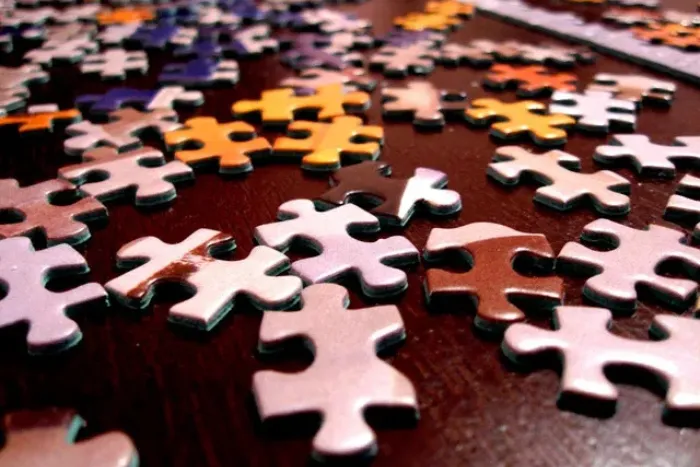 A pile of scattered, multi-colored jigsaw puzzle pieces lying on a dark wooden surface.