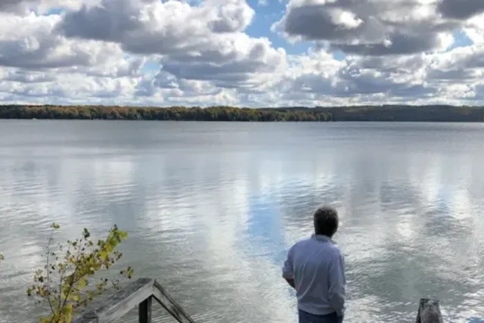 A man looking in a calm lake or reservoir reflecting the sky.